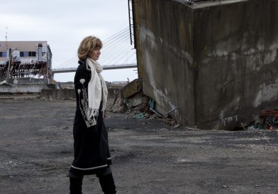 Adi Roche of Chernobyl Children International walking by destroyed buildings seaside in Soma City, Fukushima Prefecture